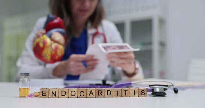 Text Endocarditis on wooden blocks and heart model on doctor desk. Woman physician examines ultrasound scan images in medical office setting