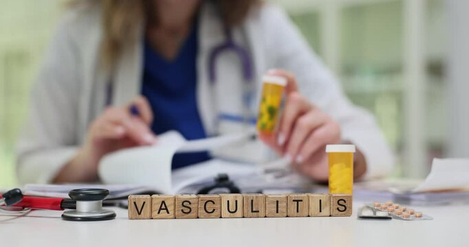 Text Vasculitis on wooden blocks and medic holding pills in bottle in clinic. Female doctor works on patient file prescribing medication in hospital