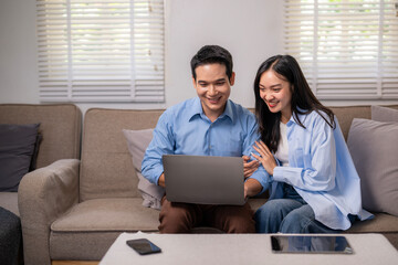 Fototapeta premium A man and woman are sitting on a couch looking at a laptop