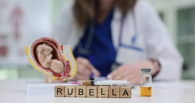 Female doctor writes prescription near anatomical model of fetus and Rubella vaccine syringe and vial on desk in clinic. Congenital rubella syndrome