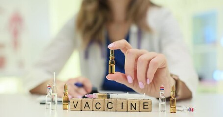 Word Vaccine on wooden cubes and doctor hand with vials at desk. Woman physician prepares medication dose at appointment in medical office setting
