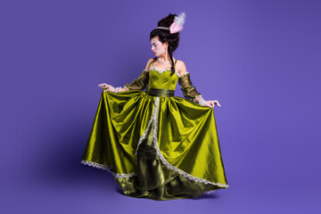 Elegant young woman in a green historic gown on a violet background exuding grace and sophistication