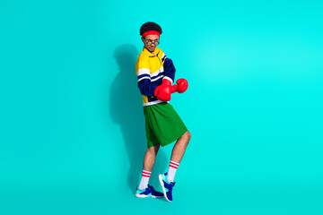 Fototapeta premium Energetic young man posing in retro activewear on teal background, boxer gloves