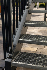 Sturdy metal stairs provide access to raised platform situated in sunny outdoor garden. The steps...