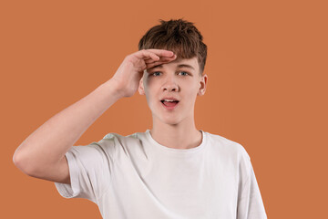 Young man saluting with a playful expression against a warm orange background during a casual...