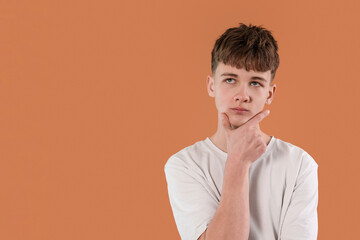 Boy thinking thoughtfully in front of an orange background during a creative brainstorming session...