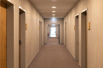 A modern hallway features a uniform design with multiple doors lining both sides. Bright lights...