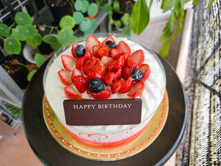 Whipped cream birthday cake topped with fresh strawberries and blueberries, with a chocolate plaque that reads "Happy Birthday."