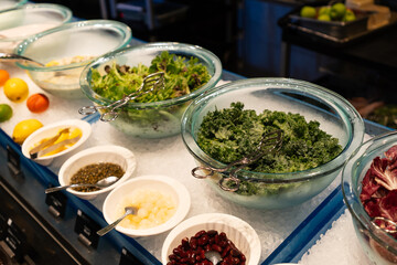 Fresh assorted greens and salad toppings in glass bowls on ice at a self-service buffet bar.