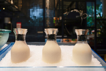 Three glass carafes of chilled milk placed on crushed ice at a breakfast buffet station.