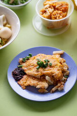 Fried carrot cake with eggs on blue plate on isolated green table background