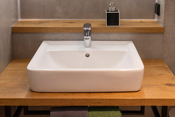 Fototapeta premium A white ceramic sink sits on a wooden countertop in a contemporary bathroom. The faucet is polished chrome, reflecting the ambient light in a streamlined setting