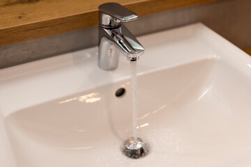 A sleek chrome faucet delivers a steady stream of clear water into a clean, white sink. The contemporary bathroom features warm wooden accents and a minimalist design, creating a refreshing space