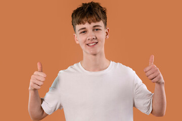 Teen boy gives a thumbs up showing positivity and confidence against a solid orange background...