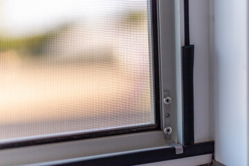 Sunlight streams through a fine mesh window screen, creating a warm and inviting indoor ambiance....