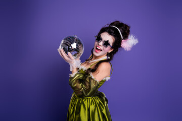 Elegant woman in vintage green dress holding a disco ball against a vibrant purple background