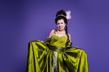 Elegant woman in historical green dress making funny expression against purple backdrop