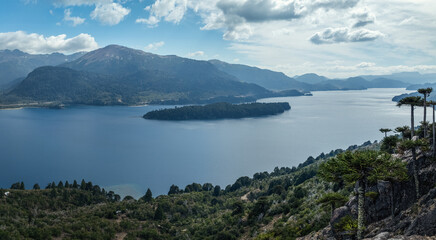 Lake Moquehue with Araucaria trees cling to a rocky cliff under a cloudy sky. Neuquen, Argentina