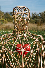 Close-up of geometric human sculpture with red heart, sitting in green field