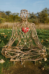 Geometric wire sculpture of meditating figure with red heart on grassy field