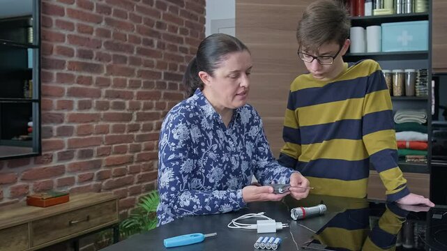 Mother teaching son how to use battery powered radio while checking emergency kit with lantern, lighter and charging cable. Family preparing 72 hours survival kit for disaster or electrical blackout.