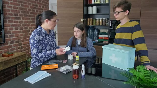 Mother teaching children how to use emergency medical supplies like injection, pills and disposable face masks. Family preparing 72 hour survival kit and checking medication stocked for disasters.