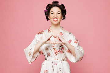 Young housewife housekeeper woman wear white robe hair rollers showing shape heart with hands...
