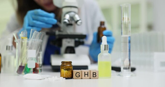 Scientific researcher wearing protective gloves examining GHB sample under high powered microscope.Gamma hydroxybutyric acid research in laboratory