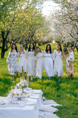 Women in white dresses stand in a field holding hands