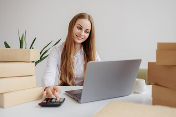 Fototapeta premium Woman working on laptop at office desk surrounded by packages during daytime