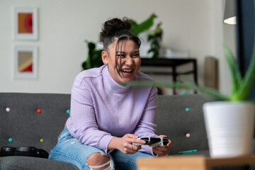 A cheerful young woman is playing video games on a couch. She is laughing and holding a controller, having fun during her leisure time indoors.
