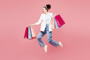 Full body side view young happy woman wear white clothes hold shopping paper package bags jump high...