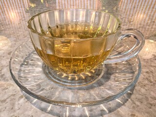 Clear glass cup of hot tea on a matching saucer.