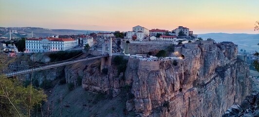 Obraz premium the iconic Sidi M'Cid Bridge and the city's dramatic cliffs. The setting sun bathes the rugged landscape and historic buildings in warm light, showcasing the 