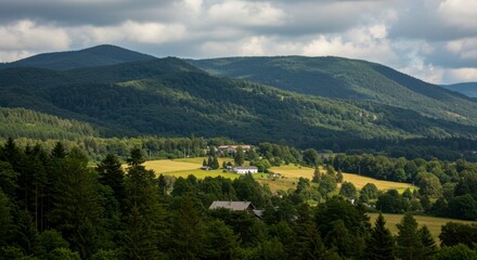 Fototapeta premium Serene valley nestled amidst verdant mountains under a partly cloudy sky. Farmland, forests, and distant hills create a picturesque landscape