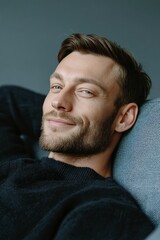 Obraz premium A confident, smiling young man with beard and mustache lounging comfortably in modern style setting.