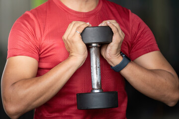 Wellness Focus. Man holding dumbbell close to chest in gym.