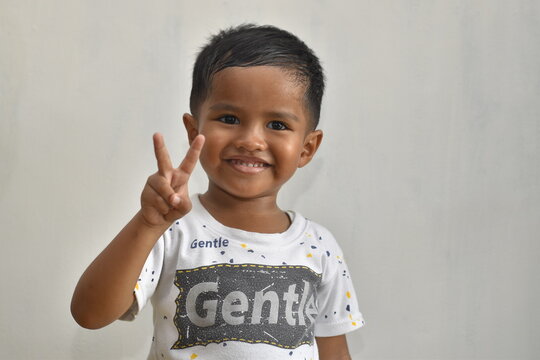 close up of 3 year old boy raising two fingers while smiling, on white background