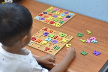 3 year old boy playing Alphabet puzzle on wooden table