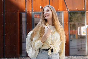 Young woman with long hair smiles while walking near modern architecture on a sunny day in a vibrant urban setting