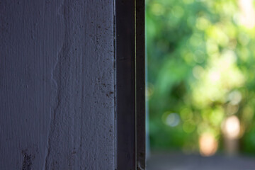 A textured grey wall and window frame stand sharply against a softly blurred green bokeh background, symbolizing a quiet view and the gentle connection between indoors and nature.

