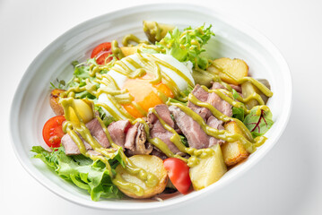 A fresh gourmet salad with mixed greens, cherry tomatoes, roasted potatoes, beef slices, and a poached egg, drizzled with green dressing, served in a white bowl.
