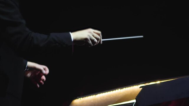 Male conductor behind the podium directing orchestra on stage with pupitre, musicians and choir, the philharmonic venue hall during concert, symphony orchestra director hands conducting waving baton