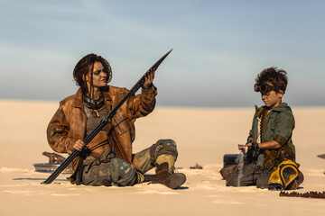 Post-Apocalyptic Woman And Boy Checking Weapons At Desert Camp Site