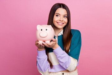 Beautiful young rich woman holding a piggy bank and smiling on a pink background