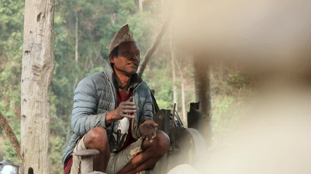 An old man is making a sickle in a traditional village blacksmith workplace. He heats the metal and shapes it with a hammer. Great for videos about rural life, tradition, or handmade tools.