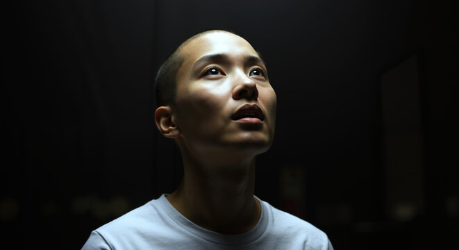 Asian man looking up contemplative expression dark background dramatic lighting. Male portrait thoughtful mood introspective meditation spiritual wellness concept