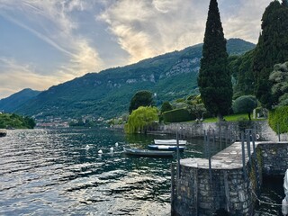 Peaceful lakeside promenade in Lenno and Ossuccio, with neatly trimmed trees, waterfront benches, mountain views, colorful villages and scenic perspectives over Lake Como