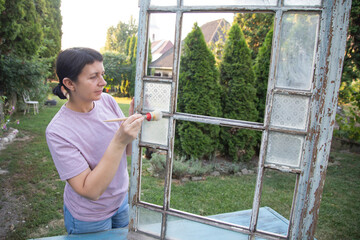 Painting a wooden vintage window outdoors, an eco-friendly re-use business.