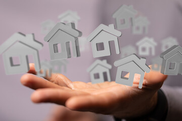 Image depicts a hand holding several 3D house models, symbolizing real estate, property, and home...